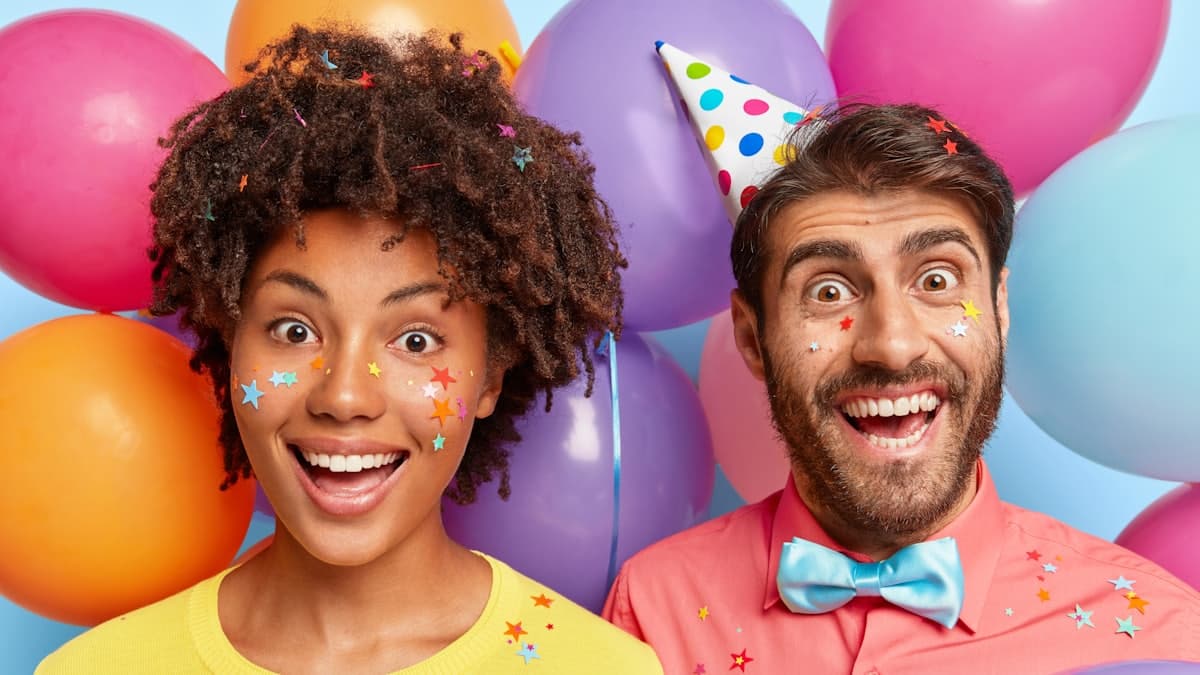 Dos personas sonriendo delante de una pared de globos en un cumpleaños