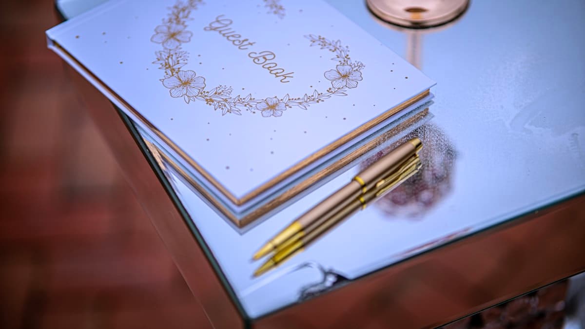 Libro de firmas con lapicera dorada sobre una superficie espejada
