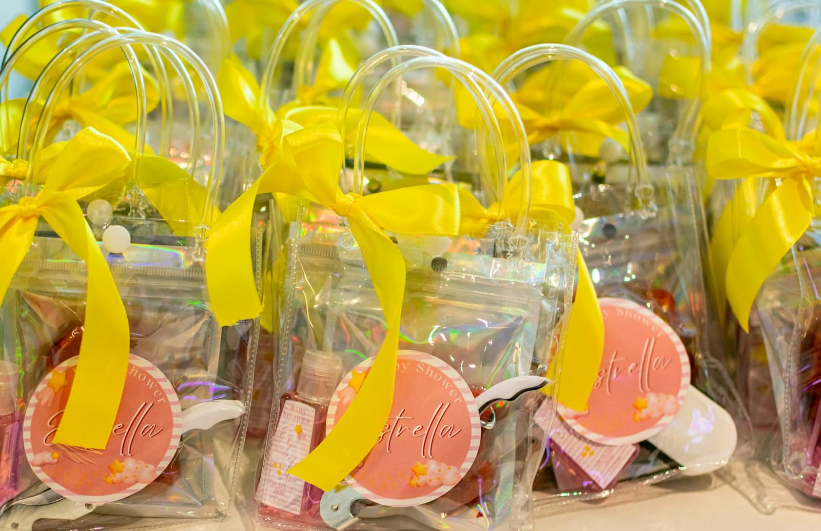 Bolsitas transparentes de cumpleaños con moño amarillo y etiqueta con el nombre, en fila sobre una mesa