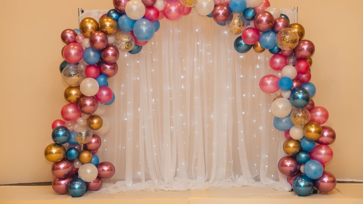 Arco de globos de colores junto a una cortina blanca