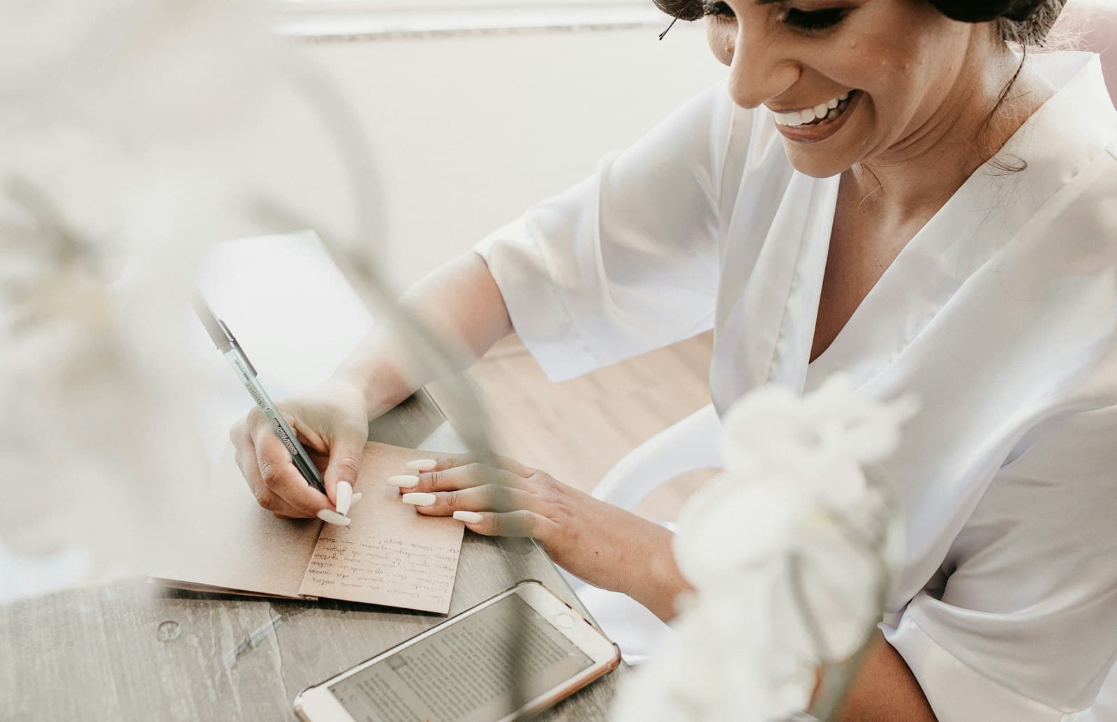 Mujer escribiendo a mano en un cuaderno sobre una mesa, con una tablet al lado