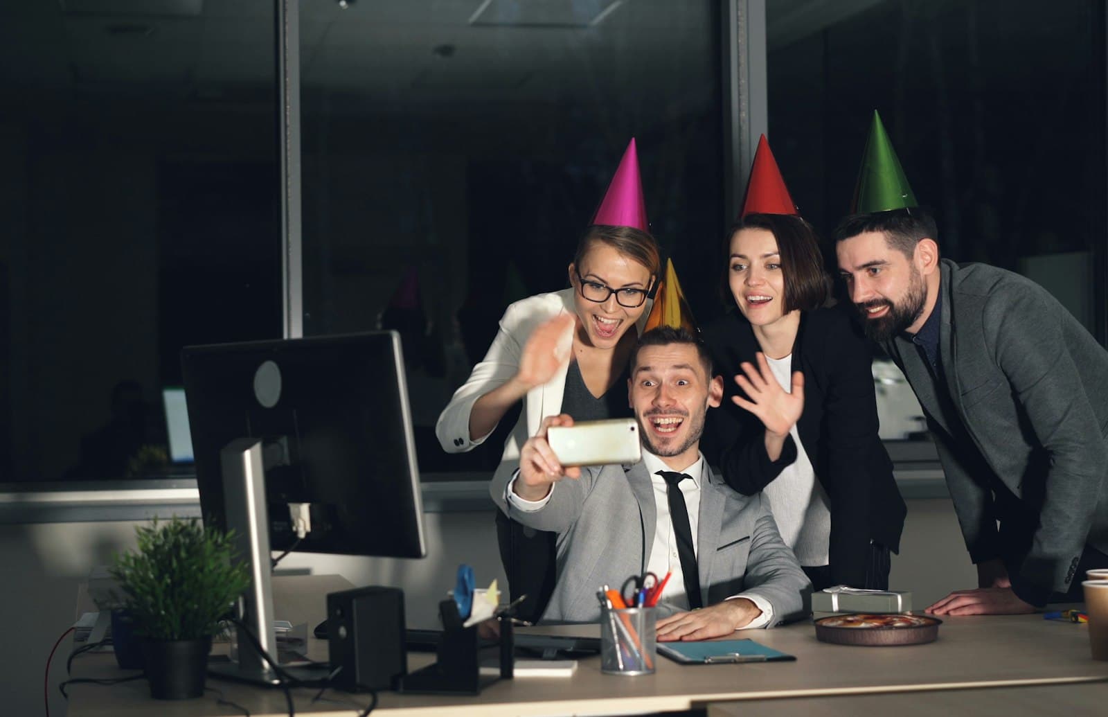 Compañeros de trabajo con gorros de fiesta sacándose una selfie en la oficina de noche
