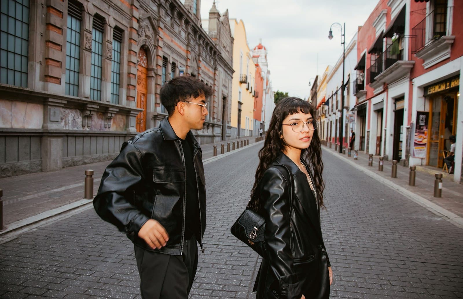 Pareja joven con camperas de cuero caminando por una calle empedrada de un casco histórico