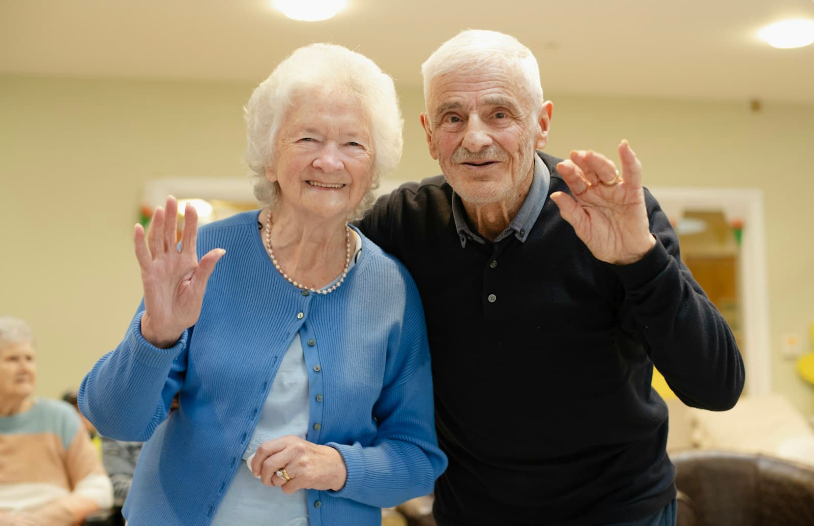 Pareja de abuelos sonriendo y saludando a la cámara en un salón familiar