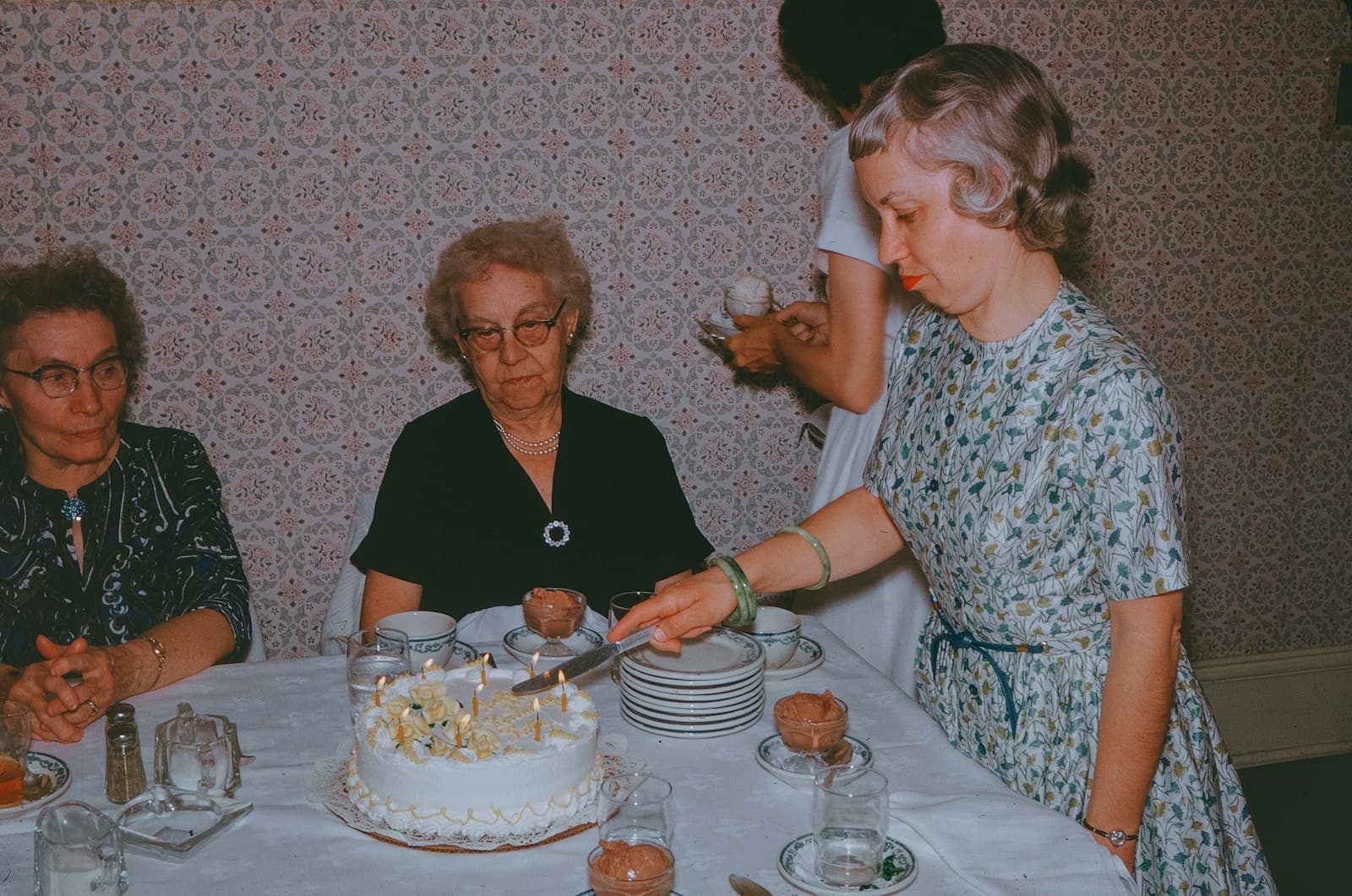 Mujer cortando una torta de cumpleaños rodeada de invitados