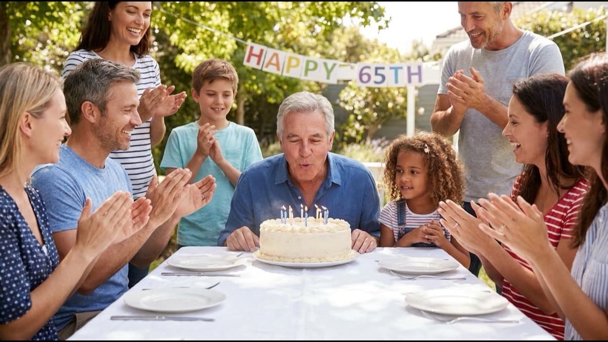 Hombre de 65 años soplando las velas de la torta rodeado de su familia