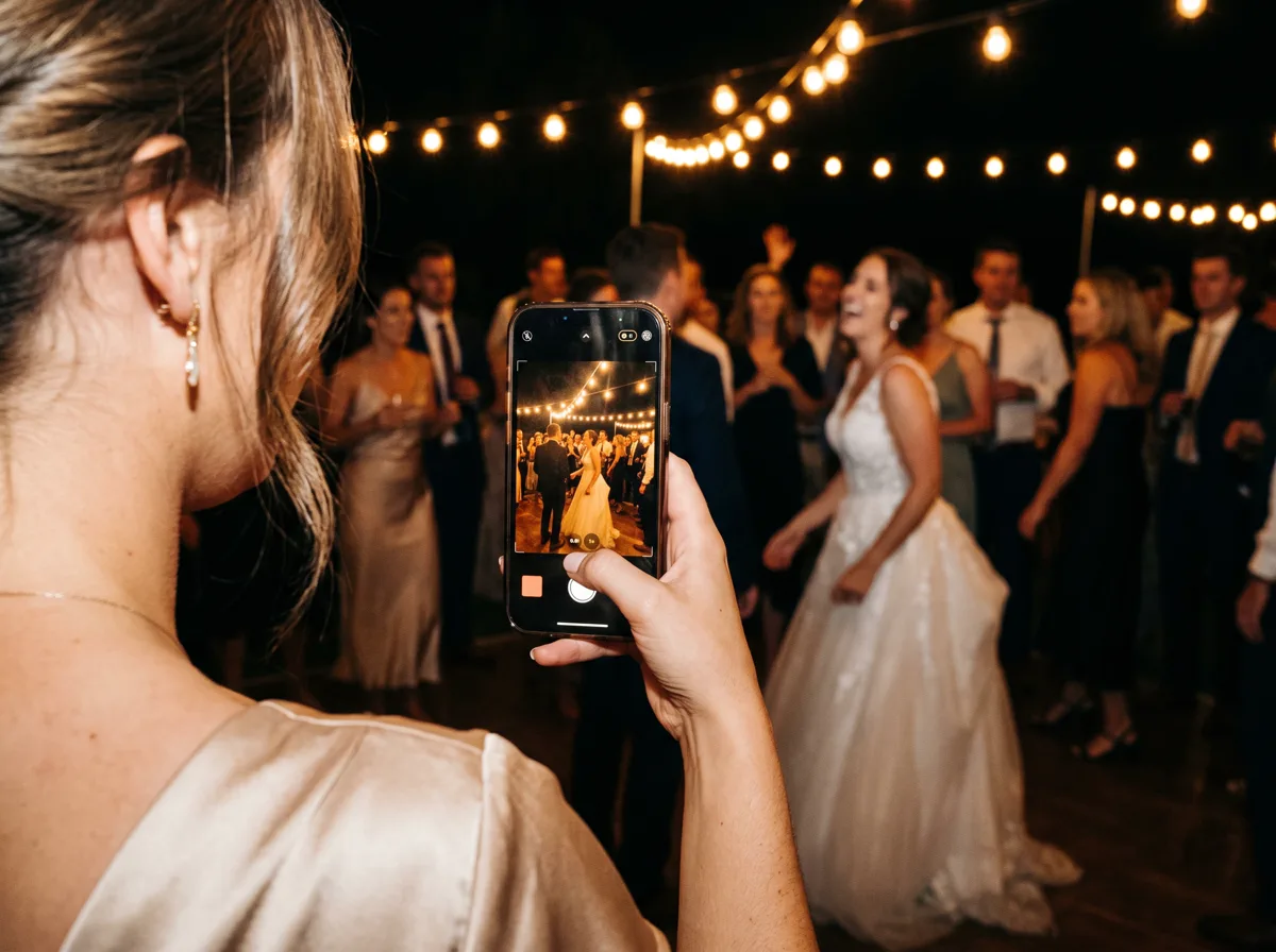 Una invitada fotografía con su celular a los novios bailando en la pista, bajo las luces colgantes.